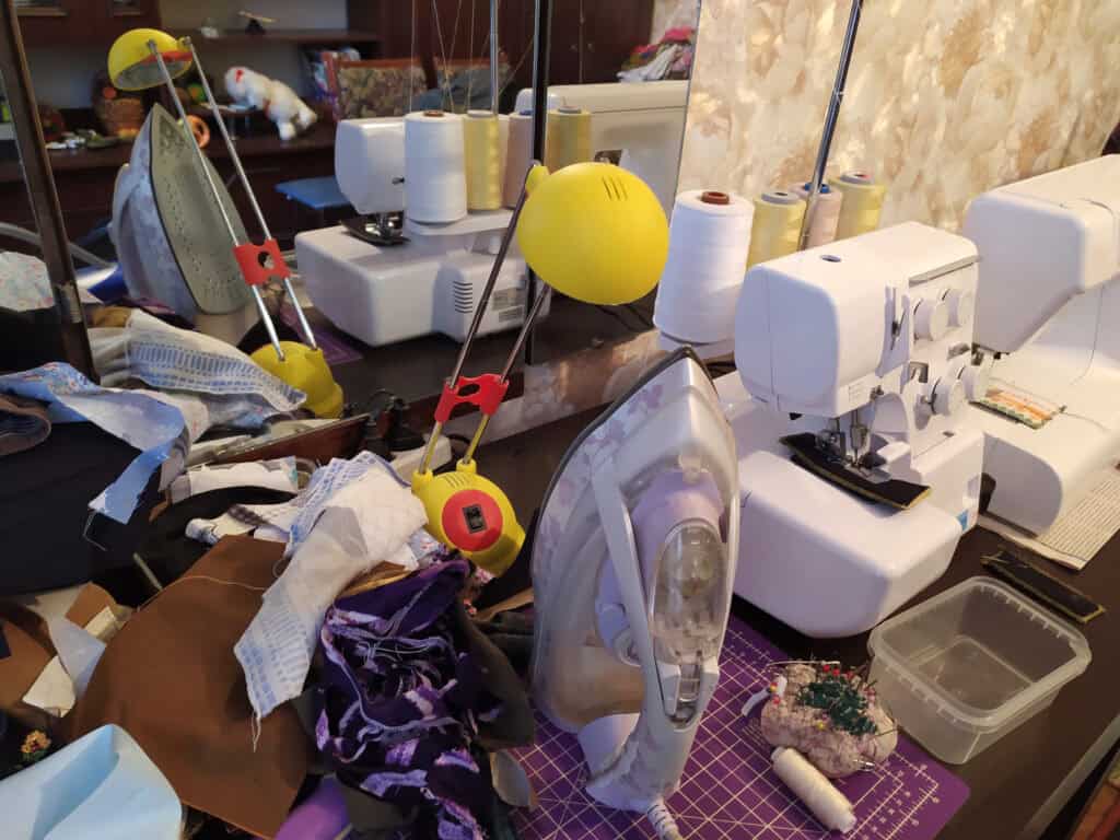 a cluttered table with a serger, iron, and random sewing items