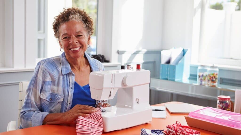 Older woman sewing on her home machine and smiling.